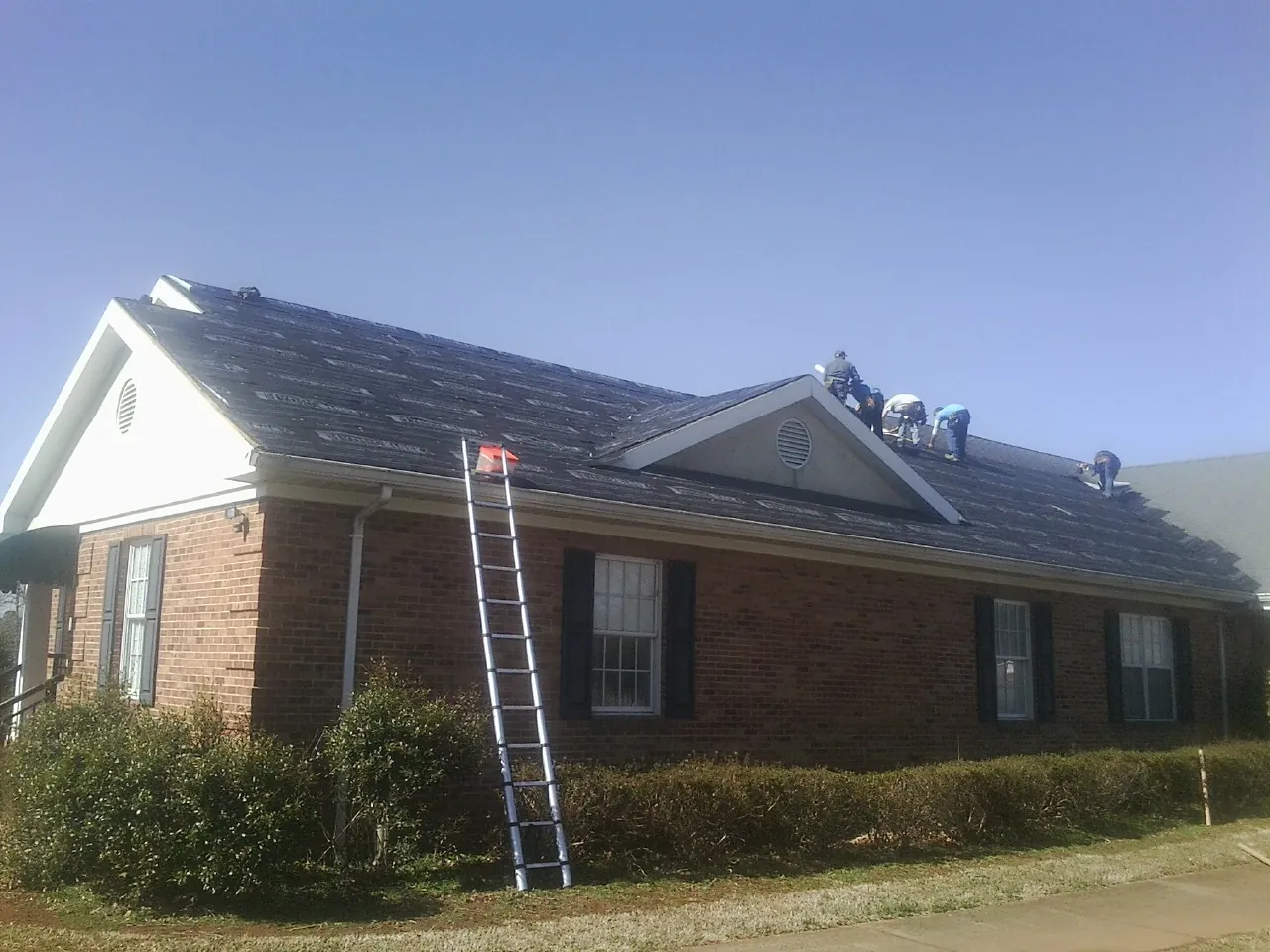 Crew tearing shingles off a brick ranch roof with a ladder set — Emergency Roof Repair work by our crew in Ashfield