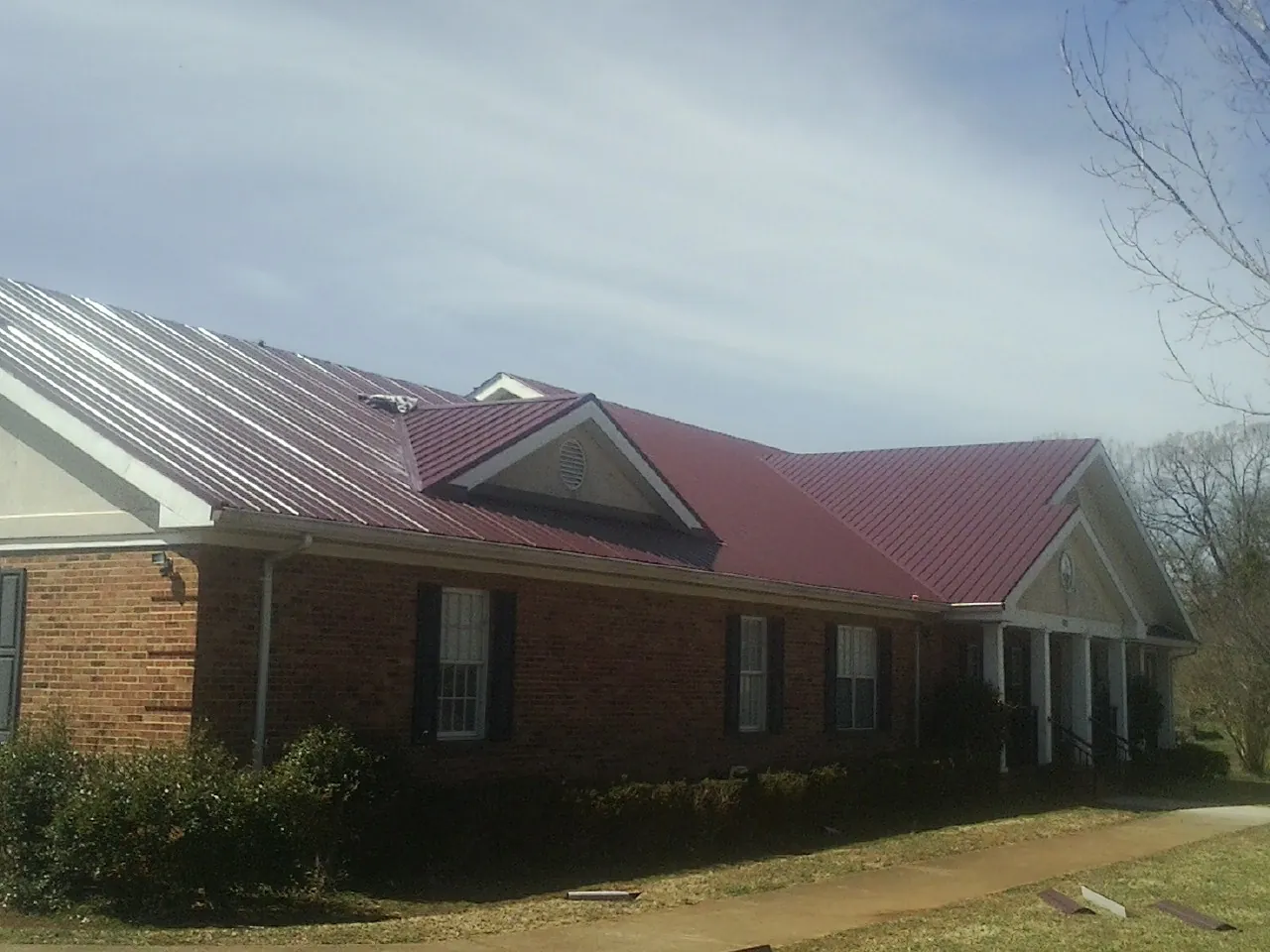 Red metal roof with gabled entries on a long brick building, from a Hail Damage Roof Repair job in Ashfield