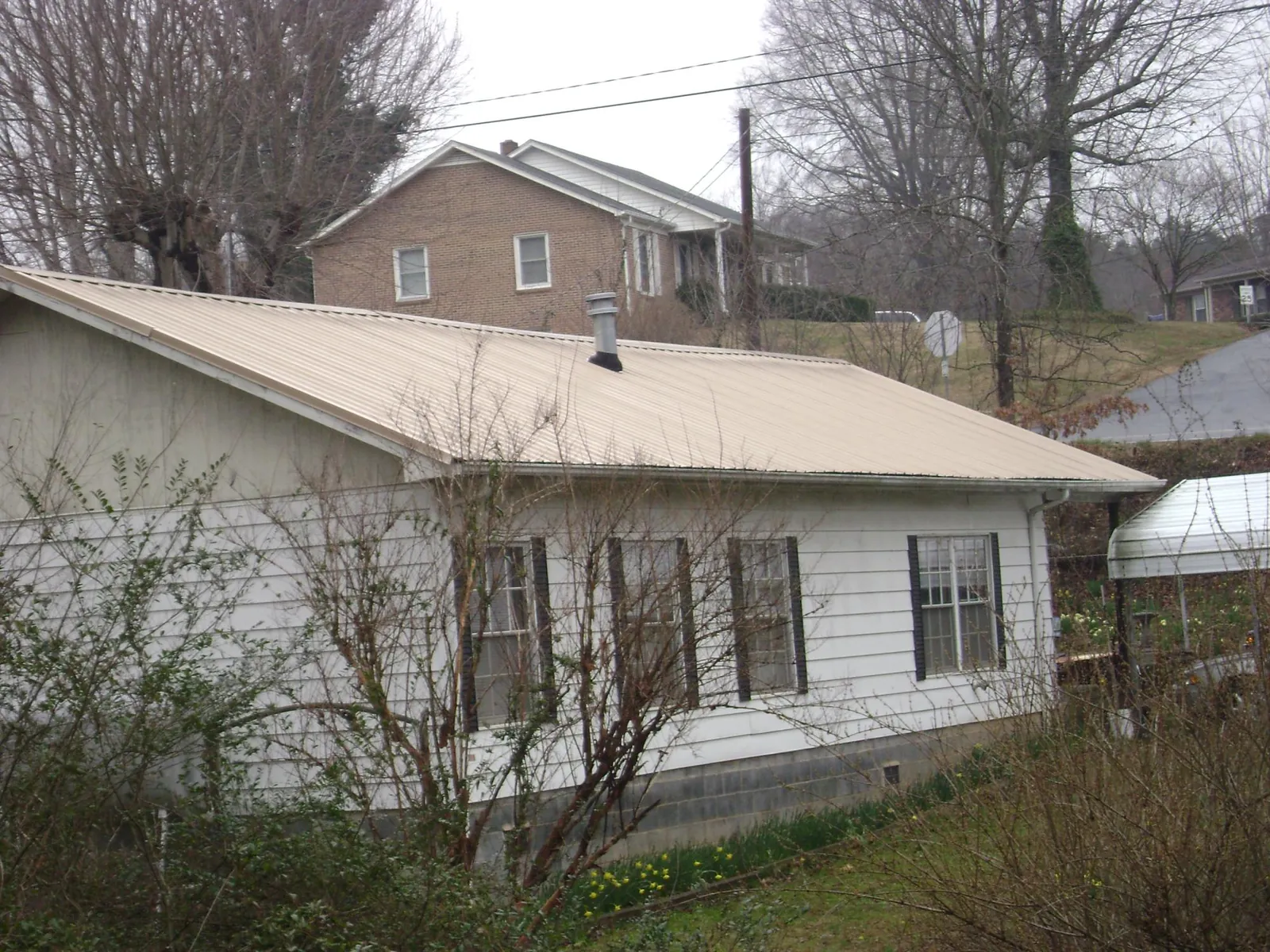 Tan metal roof on a white sided house set into a hillside — Commercial Roofing by Roofing Brothers in Ashfield